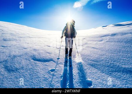 Un tour sciistico che sale in salita verso un sole luminoso sulle montagne del Jotunheim in Norvegia Foto Stock