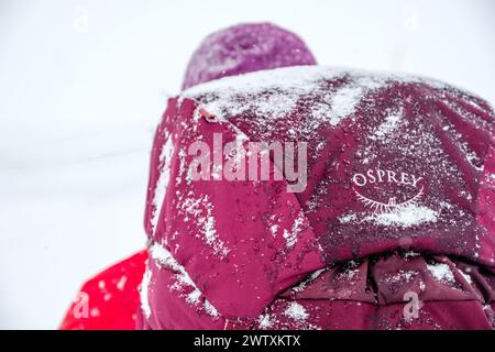 Uno zaino invernale che porta con sé uno zaino Osprey con una spolverata di neve Foto Stock