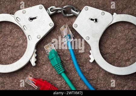 Vista dall'alto delle manette e dei cavi del computer, concetto sul tema della punizione nel campo dei crimini informatici Foto Stock