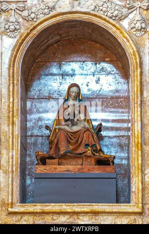 La Vergine, seduta sul sella curulis, ha le mani strette e il viso piegato sul bambino, che giace in grembo. Saturnino gatti. L'Aquila, Italia Foto Stock