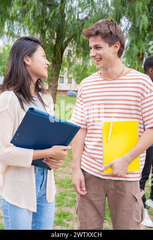 Amici sorridenti del college che guardano appunti, parlano e ridono nel campus.verticale Foto Stock