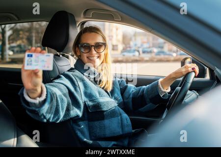 donna che mostra la sua nuova patente mentre è seduta in macchina. scuola guida Foto Stock