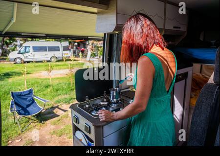 Cucinare caffè in camper, camper o camper durante il viaggio in campeggio. Una donna prepara il caffè al mattino durante una vacanza in famiglia in campeggio o in campeggio Foto Stock