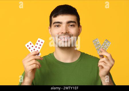 Giovane uomo con bolle di pillole di vitamina A su sfondo giallo, primo piano Foto Stock