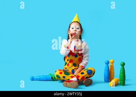 Divertente bambina in costume da clown con fischio di festa e giocoleria su sfondo blu. Festa del Fool's Day di aprile Foto Stock