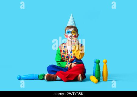 Simpatico ragazzino in costume da clown con fischio di festa e giocoleria su sfondo blu. Festa del Fool's Day di aprile Foto Stock