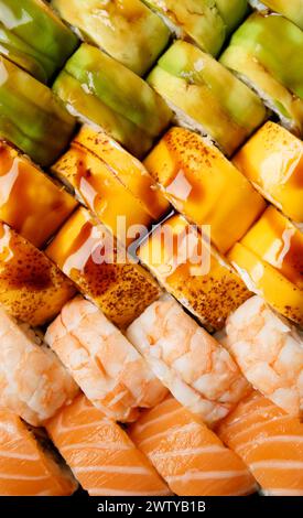 Set di sushi multicolori luminosi con salmone, gamberi, avocado, formaggio, vista dall'alto, primo piano. Viene visualizzato come sfondo. Foto Stock