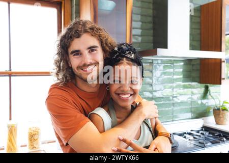 Una coppia variegata condivide un caldo abbraccio in una cucina moderna a casa Foto Stock