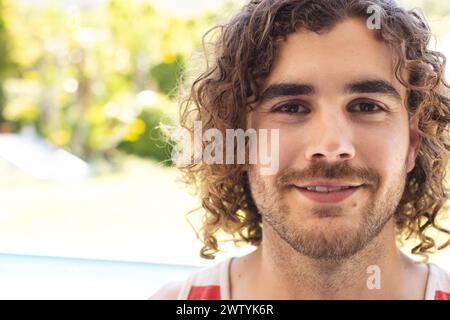 Un giovane uomo caucasico con i capelli ricci sorride calorosamente all'aperto con spazio per copiare Foto Stock