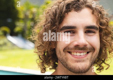 Un giovane uomo caucasico sorride all'aperto, mostrando i capelli ricci castani a casa Foto Stock