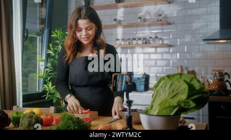 La donna in grembiule in piedi in cucina registra su smartphone il nuovo videoblog alimentare. Donna che taglia verdure su un tagliere, blogging, uno stile di vita sano Foto Stock
