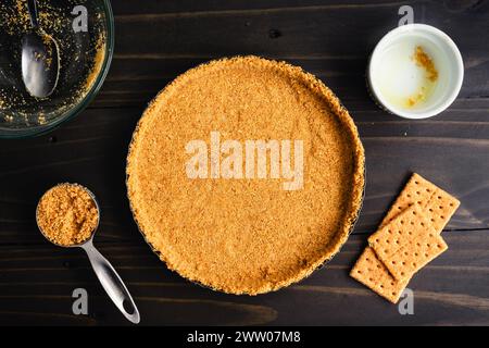 Crosta cruda di biscotti Graham non cotta in una teglia per crocchette: Crosta di biscotti graham appena sfornata, circondata da utensili da cucina e ingredienti extra Foto Stock