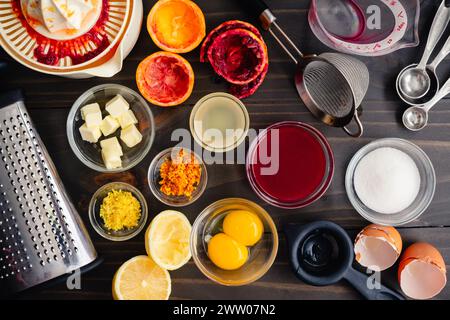 Vista dall'alto degli ingredienti preparati per la cagliata d'arancia di sangue: Succo di agrumi e scorza con tuorli d'uovo, burro e altri ingredienti e utensili da cucina Foto Stock