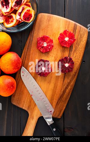 Arance sanguigne sbucciate e deseminate su un tagliere di legno: Arance pelate, tagliate a metà e intere di lamponi con un coltello dello chef e bucce laterali Foto Stock