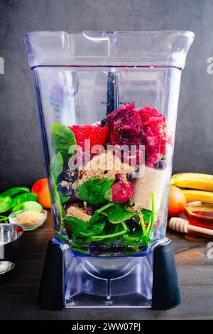 Frullato di frutti di bosco misti di arancia rossa in un frullatore a caraffa: Frutta fresca e surgelata non miscelata, foglie di spinaci, semi di lino dorati e miele Foto Stock