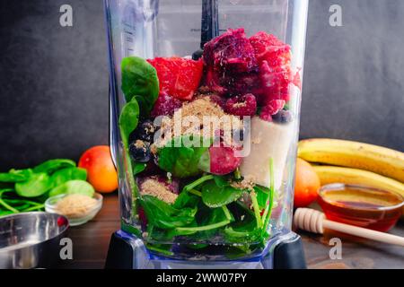 Frullato di frutti di bosco misti di arancia rossa in un frullatore a caraffa: Frutta fresca e surgelata non miscelata, foglie di spinaci, semi di lino dorati e miele Foto Stock