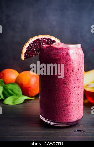 Frullato di frutti di bosco misti di arancia sangue con ingredienti: La colazione appena preparata è soffice con arance rosse e foglie di spincah per bambini sullo sfondo Foto Stock