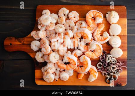 Pesce in camicia disposto su un tagliere di legno: Gamberi piccoli e grandi cucinati, calamari a fette e capesante su un tagliere di legno Foto Stock