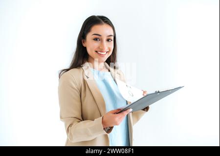 Bella bruna indiana o araba, consulente finanziario, segretaria, si erge su sfondo bianco isolato, tenendo una cartella con documenti e grafici, guarda la macchina fotografica, sorridi Foto Stock