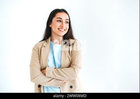 Splendida donna bruna indiana o araba con un'elegante tuta, in piedi su sfondo bianco isolato con le braccia incrociate, guardando lontano, sorridendo felicemente Foto Stock