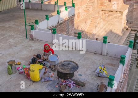 Jodhpur, Rajasthan, India - 17 dicembre 2023: Una donna anziana che cucinava su firer accanto al Tooji, sta bene con un uomo e un ragazzo Foto Stock