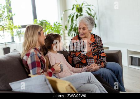 Tre generazioni di donne si divertono a ridere e conversare su un comodo divano del salotto Foto Stock