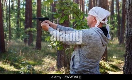 Un uomo nella foresta tra gli alberi, che sparava con la pistola tedesca. Foto Stock