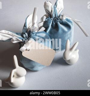 Cartolina di Pasqua. Due borse regalo creative con orecchie coniglietti e piccoli coniglietti bianchi in ceramica su sfondo grigio. Confezione regalo fai da te per Pasqua. Mock-up. Co Foto Stock