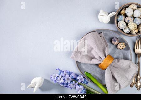 Elegante tavolo pasquale per caffetterie e ristoranti in grigio. Tovagliolo, uova di quaglia, posate d'annata, stoviglie bellissime, fiore viola del martinetto, ceram Foto Stock