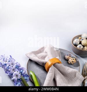 Tavola di Pasqua servita con eleganti stoviglie grigie, tovagliolo, uova di quaglia, posate vintage, fiore viola di Giacinto su sfondo grigio neutro. Primo piano. Squar Foto Stock