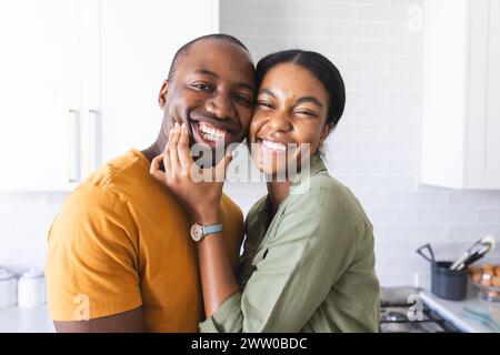 Una coppia variegata condivide un gioioso abbraccio in cucina a casa Foto Stock