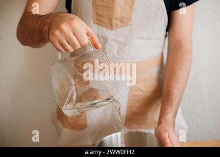 il panettiere maschile versa l'acqua in una ciotola di farina. Foto di alta qualità Foto Stock