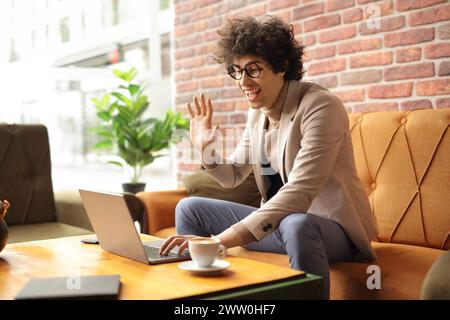 Giovane uomo in un bar che sventola di fronte a un computer portatile, concetto di tecnologia per videochiamate Foto Stock