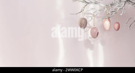 Ramo d'albero con uova di Pasqua su sfondo rosa con luce solare e ombre Foto Stock