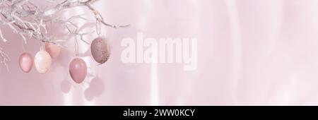 Ramo d'albero con uova di Pasqua su sfondo rosa con luce solare e ombre Foto Stock