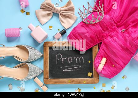 Lavagna con testo PROM, abbigliamento femminile e cosmetici su sfondo blu Foto Stock