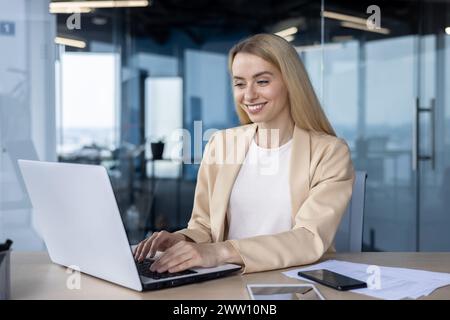 Un'allegra donna d'affari sta utilizzando un notebook in un ufficio moderno, mostrando produttività e soddisfazione. Foto Stock