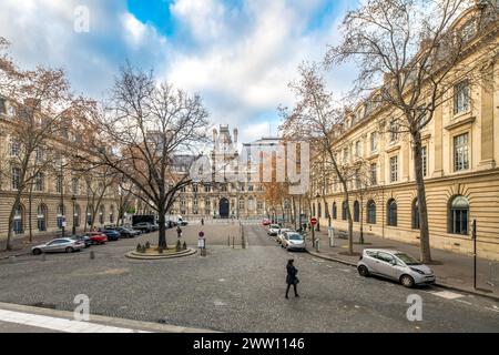 Una persona cammina attraverso una piazza alberata di Saint-Gervais-Saint-Protais con l'Hôtel de Ville di Parigi sullo sfondo. Foto Stock