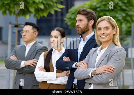 Un gruppo di quattro diversi professionisti aziendali si è schierato con fiducia fuori da un edificio di uffici, rappresentando il lavoro di squadra e la leadership. Foto Stock