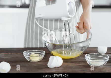 Una donna in grembiule mescola proteine di uova con un mixer elettrico, concetto di panetteria per la casa Foto Stock