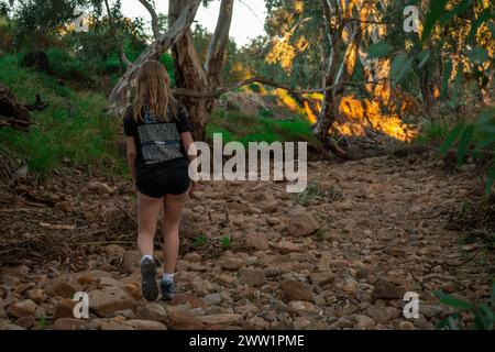 Una giovane donna contempla la natura, in piedi su un sentiero di un fiume sassoso in un'area boscosa. Foto Stock