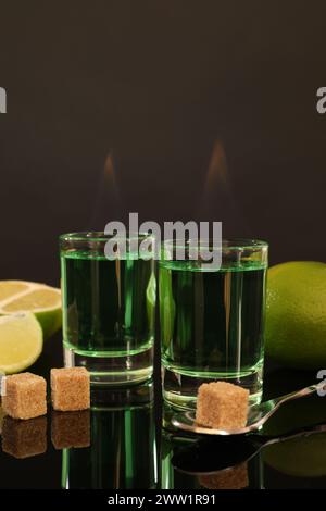 Assenzio fumante nei bicchieri da shot, zucchero di canna, lime e cucchiaio sul tavolo a specchio. Bevanda alcolica Foto Stock