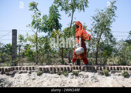 Una donna vista andare in uno stagno per raccogliere acqua potabile a Shyamnagar Gabura nel distretto di Satkhira. Nel Gabura Union, distretto di Shatkhira, nel Bangladesh meridionale, i residenti stanno affrontando una terribile crisi di acqua potabile esacerbata dai cambiamenti climatici. Le persone, comprese donne e bambini, devono percorrere quotidianamente lunghe distanze per accedere a fonti di acqua sicure, aumentando i rischi per la salute derivanti dalle malattie trasmesse dall'acqua. I dati a livello di distretto costiero evidenziano percentuali significative che si trovano a fronteggiare la carenza di acqua, mentre gli ambientalisti suggeriscono che la situazione è più grave. Il calo dei livelli dell'acqua sotterranea rende anche dee Foto Stock