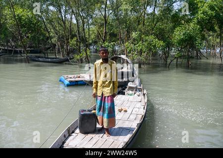 Un pescatore posa per un ritratto con un litro di acqua potabile prima di andare a pescare nella foresta di Sundarbans. Nel Gabura Union, distretto di Shatkhira, nel Bangladesh meridionale, i residenti stanno affrontando una terribile crisi di acqua potabile esacerbata dai cambiamenti climatici. Le persone, comprese donne e bambini, devono percorrere quotidianamente lunghe distanze per accedere a fonti di acqua sicure, aumentando i rischi per la salute derivanti dalle malattie trasmesse dall'acqua. I dati a livello di distretto costiero evidenziano percentuali significative che si trovano a fronteggiare la carenza di acqua, mentre gli ambientalisti suggeriscono che la situazione è più grave. Diminuzione del livello dell'acqua sotterranea rende Foto Stock