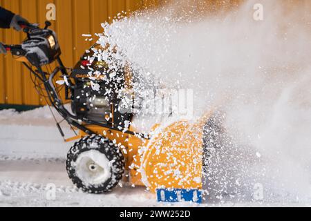 Lavoratore irriconoscibile che utilizza spazzaneve per eliminare la neve dalla strada dopo la tempesta invernale. L'operatore sta soffiando neve dopo la tormenta. Messa a fuoco selettiva Foto Stock