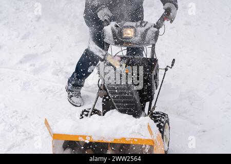 Una persona non identificata sta azionando uno spazzaneve per eliminare la neve da una strada invernale, con l'aiuto di uno spazzaneve, dopo una tempesta di neve invernale Foto Stock