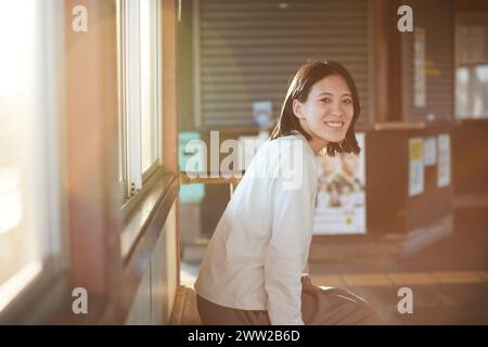 Una donna seduta su una piattaforma del treno con il sole che splende attraverso la finestra Foto Stock