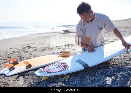 Un uomo seduto sulla spiaggia con una tavola da surf Foto Stock