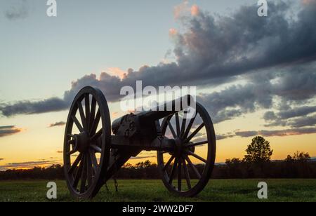 Una silhouette a bassa angolazione mostra un cannone con ruote a raggi contro nuvole scure e un bagliore arancione al Manassas National Battlefield Park, Virginia. Foto Stock