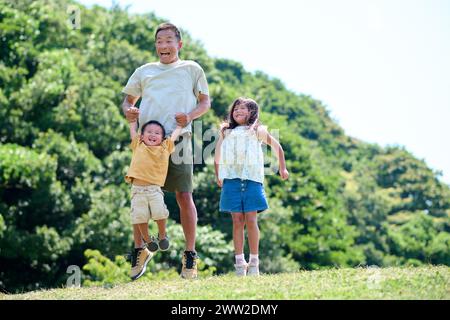 Un uomo e due bambini che saltano sull'erba Foto Stock